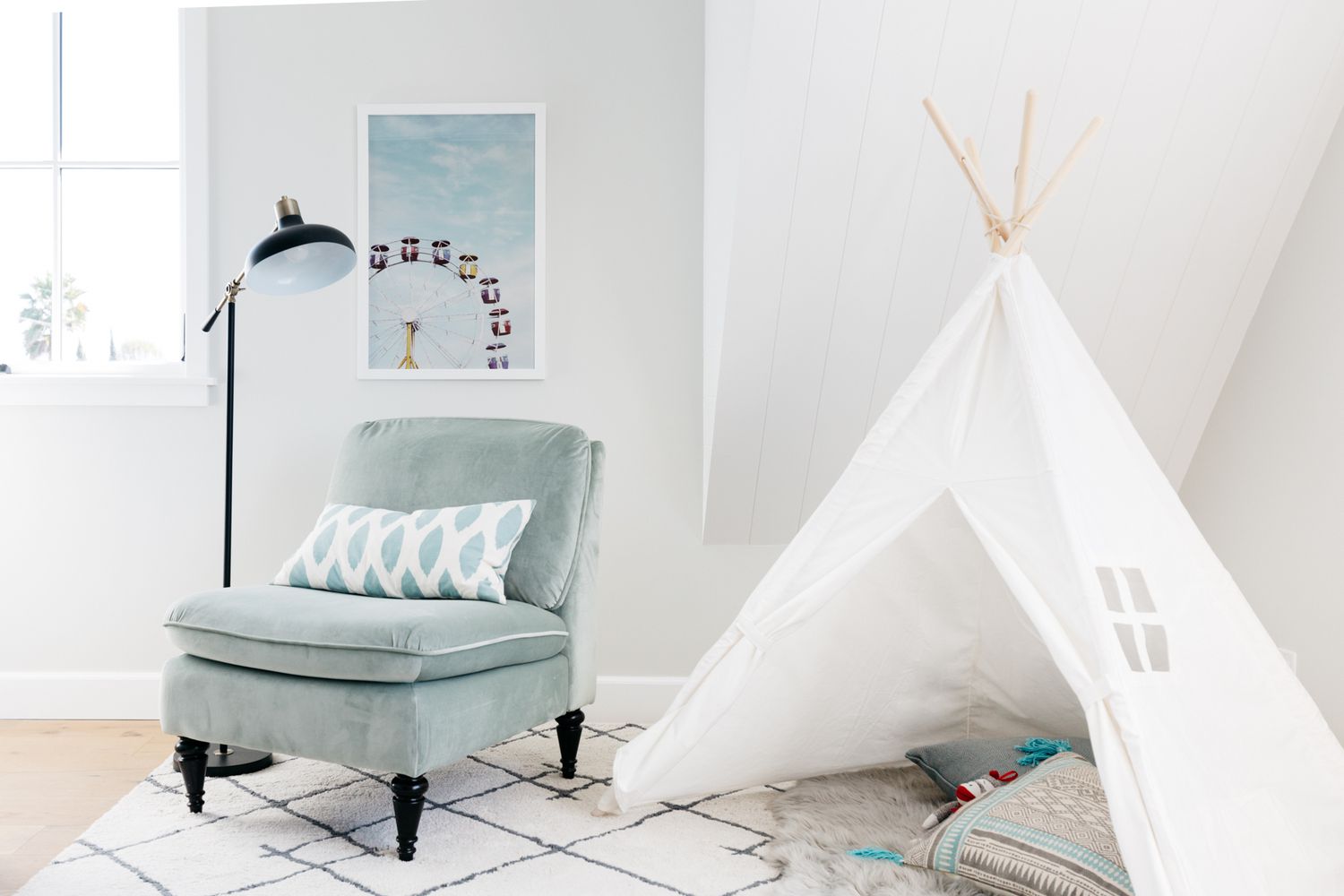 Tipi blanc installé dans la chambre d'enfant à côté d'une chaise et d'une lampe vert clair avec des murs blancs autour