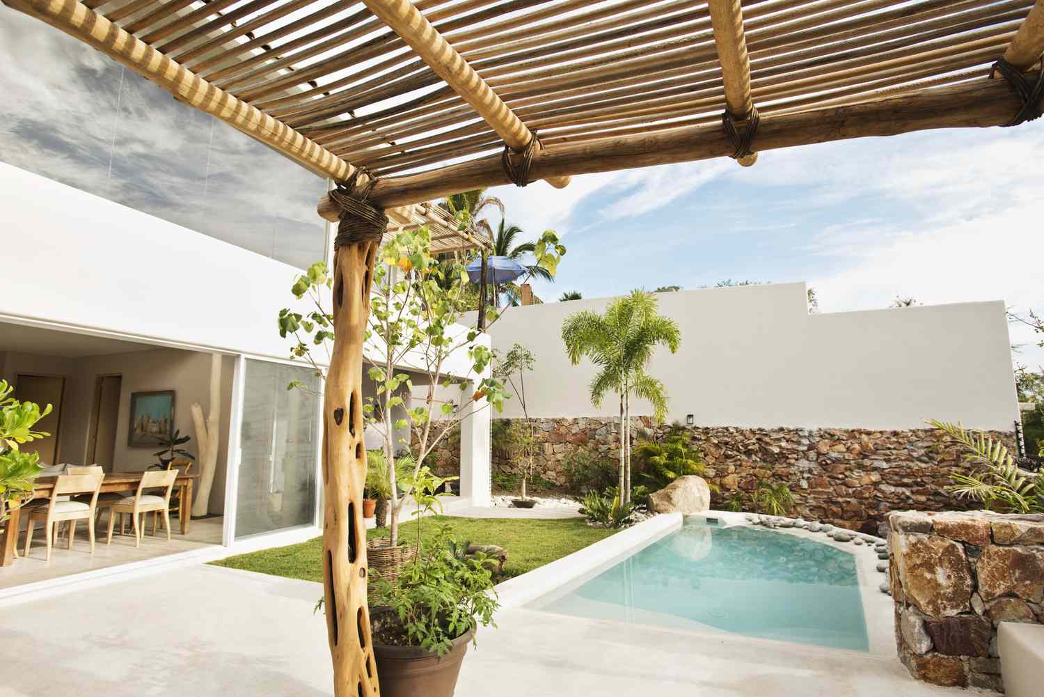 Vista de uma piscina no quintal com um pequeno muro de pedra e uma pérgula de madeira.