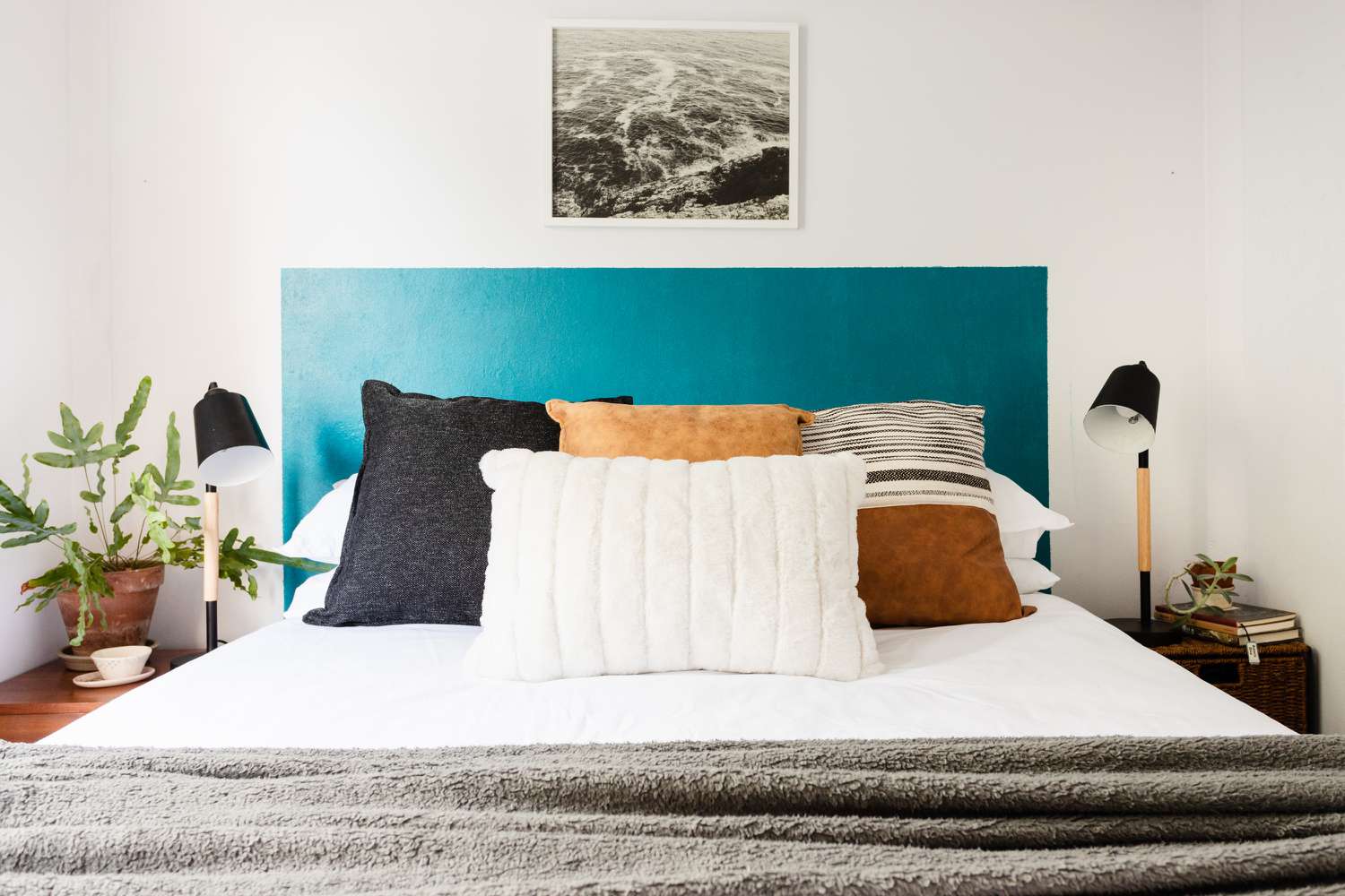 Cabecero DIY azul cerceta detrás de la cama con cojines blancos, marrones y negros