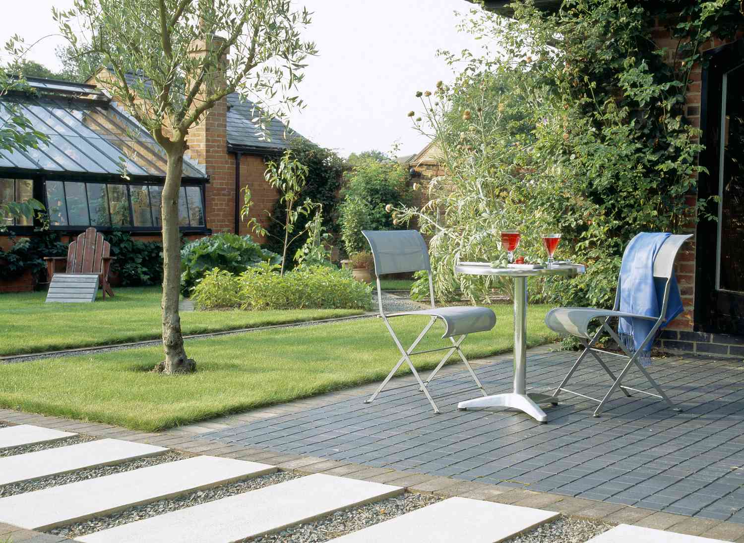 Patio de estilo moderno con sillas y mesa de metal, junto a elegante pasarela.