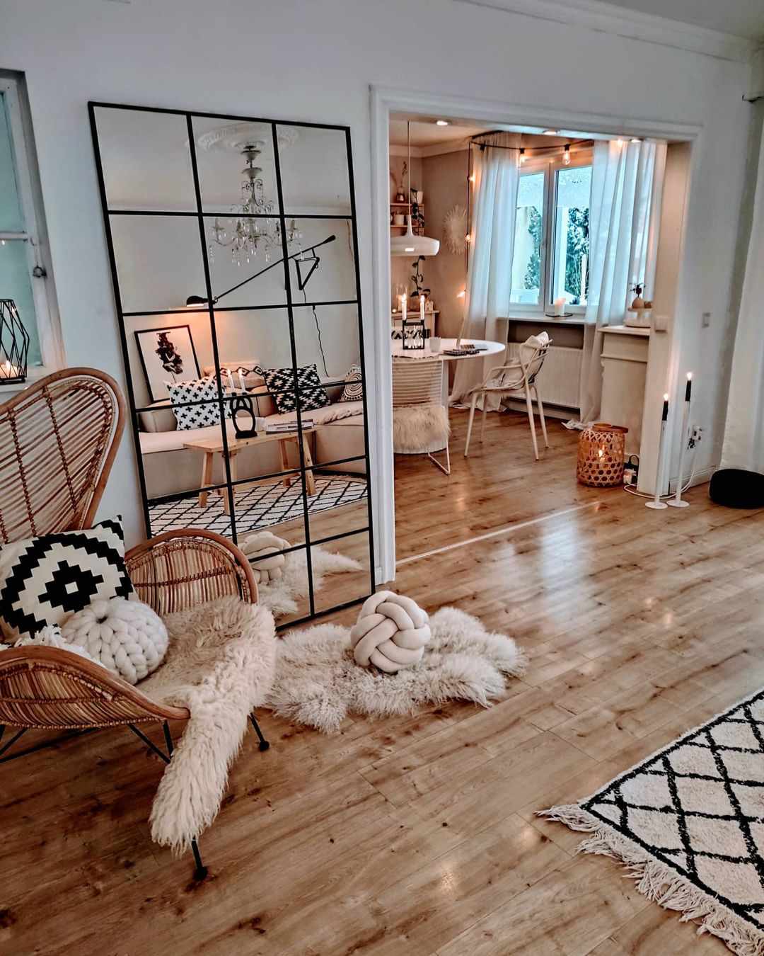 Un coin salon cosy avec un grand miroir DIY, un tapis en fausse fourrure et une chaise en rotin.