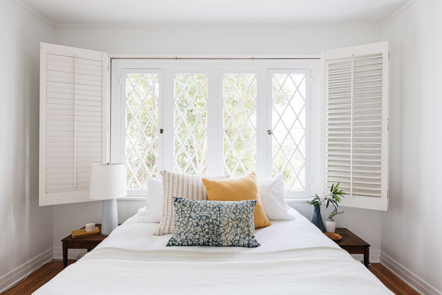 Chambre à coucher sans tête de lit devant des fenêtres ouvertes avec des coussins