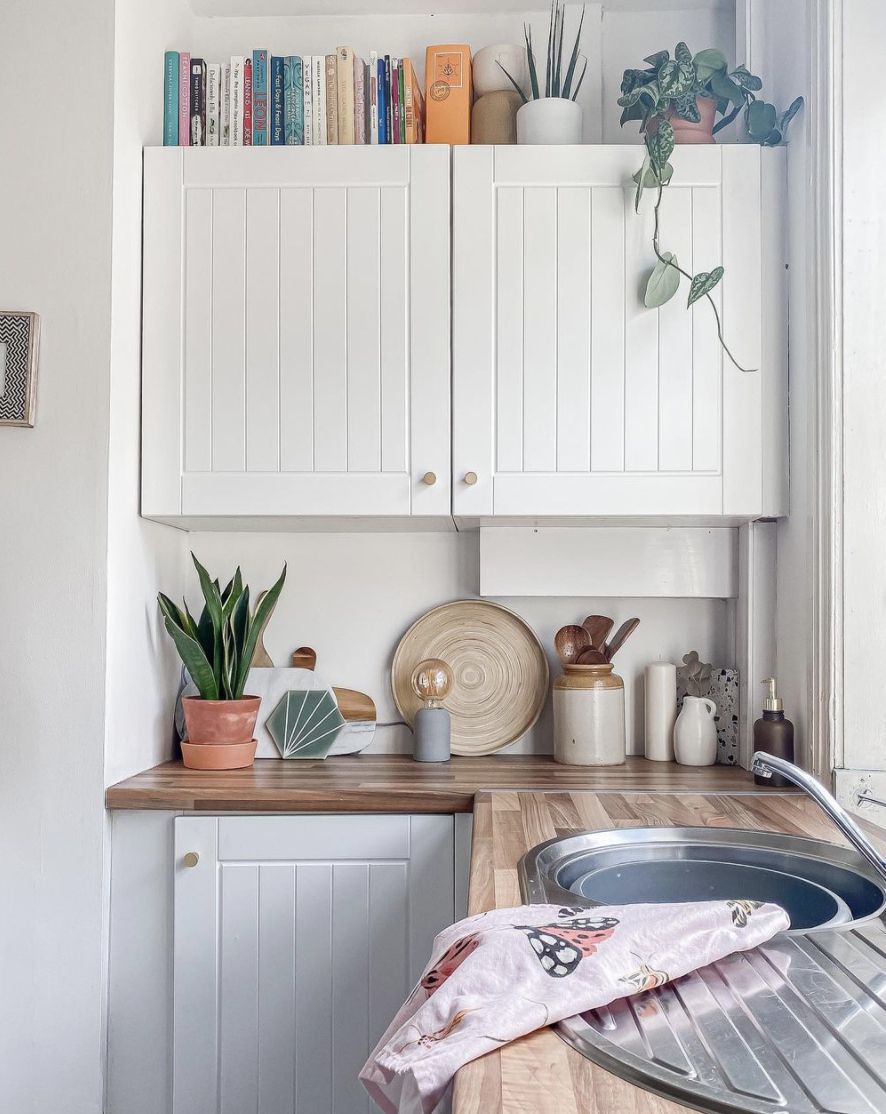 cozinha com armários brancos e livros de receitas e plantas colocados em cima