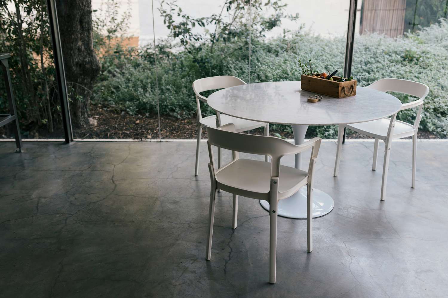 Moderne Bauernhaus-Glasküche mit drei Plastikstühlen und Tisch auf Betonboden