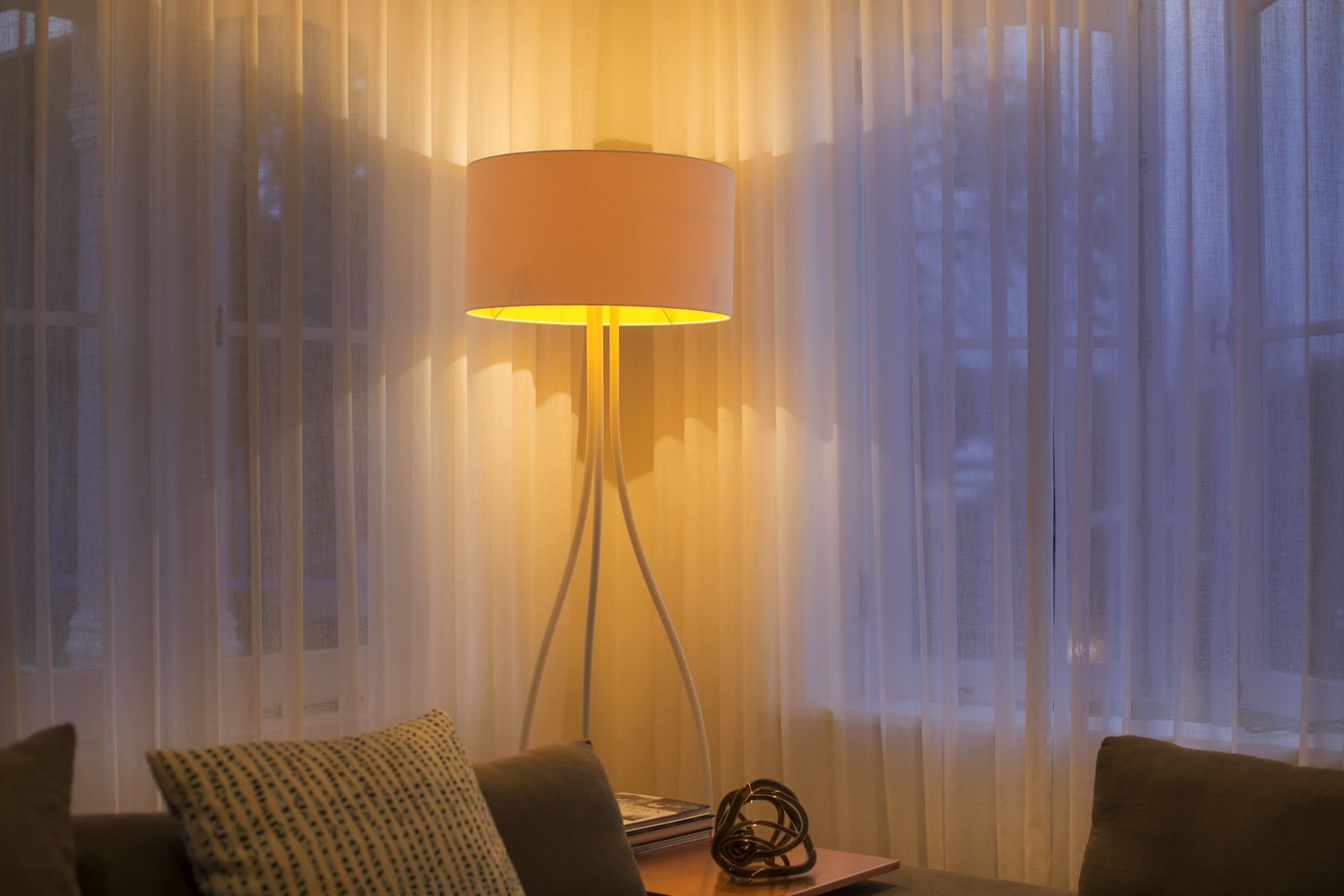 Lámpara de pie iluminada en la ventana con cortinas transparentes
