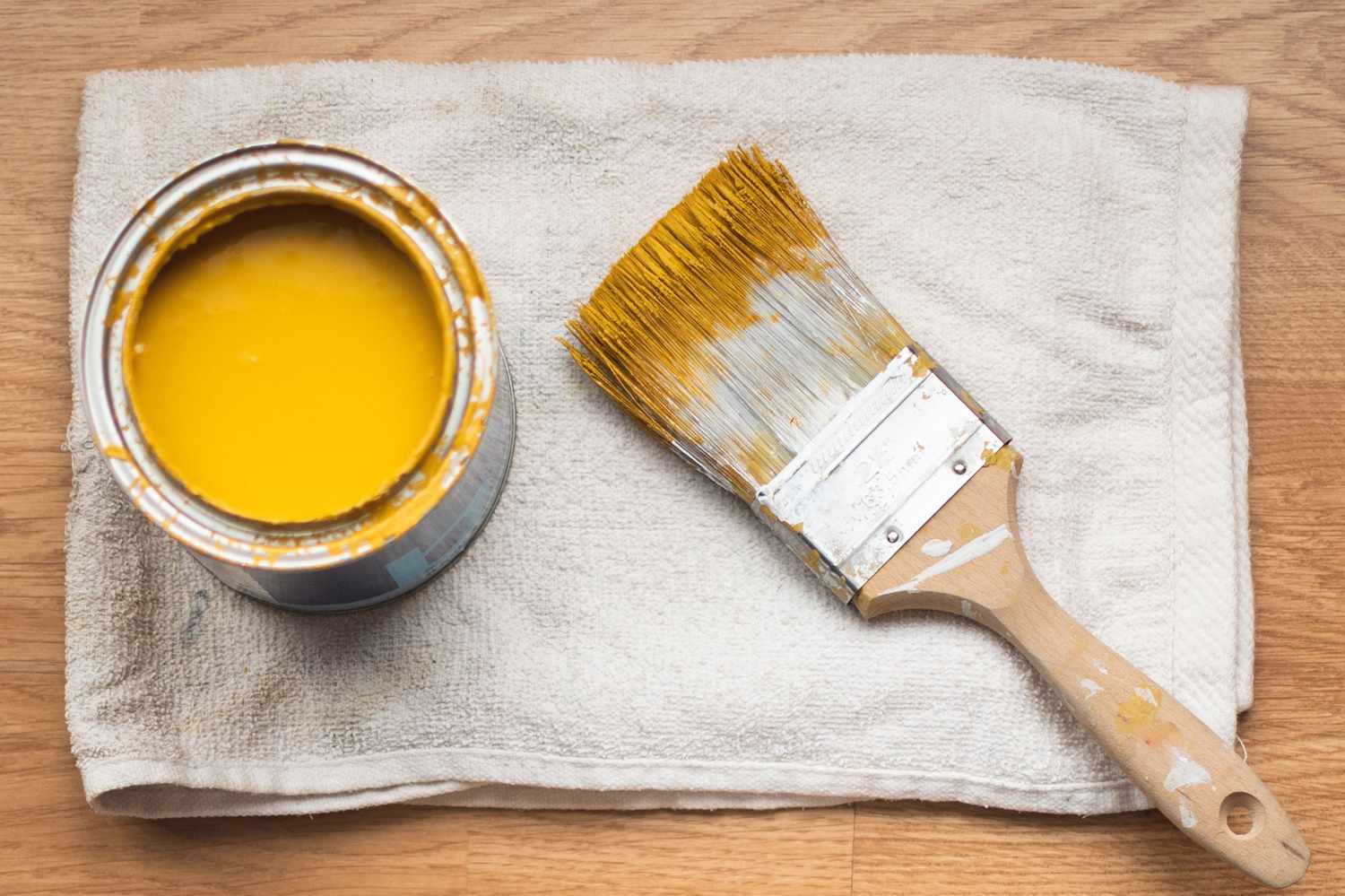 Farbeimer mit gelber Farbe und Pinsel auf weißem Lappen