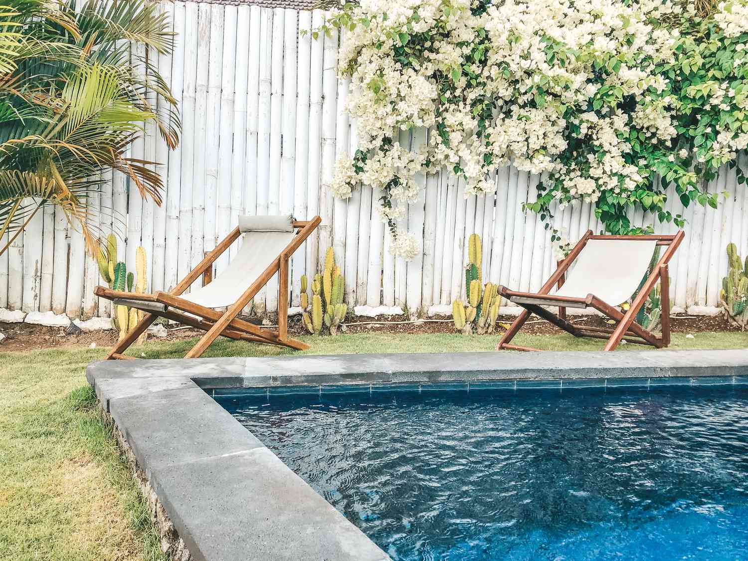 Uma piscina no quintal cercada por uma cerca de bambu branco e espreguiçadeiras.