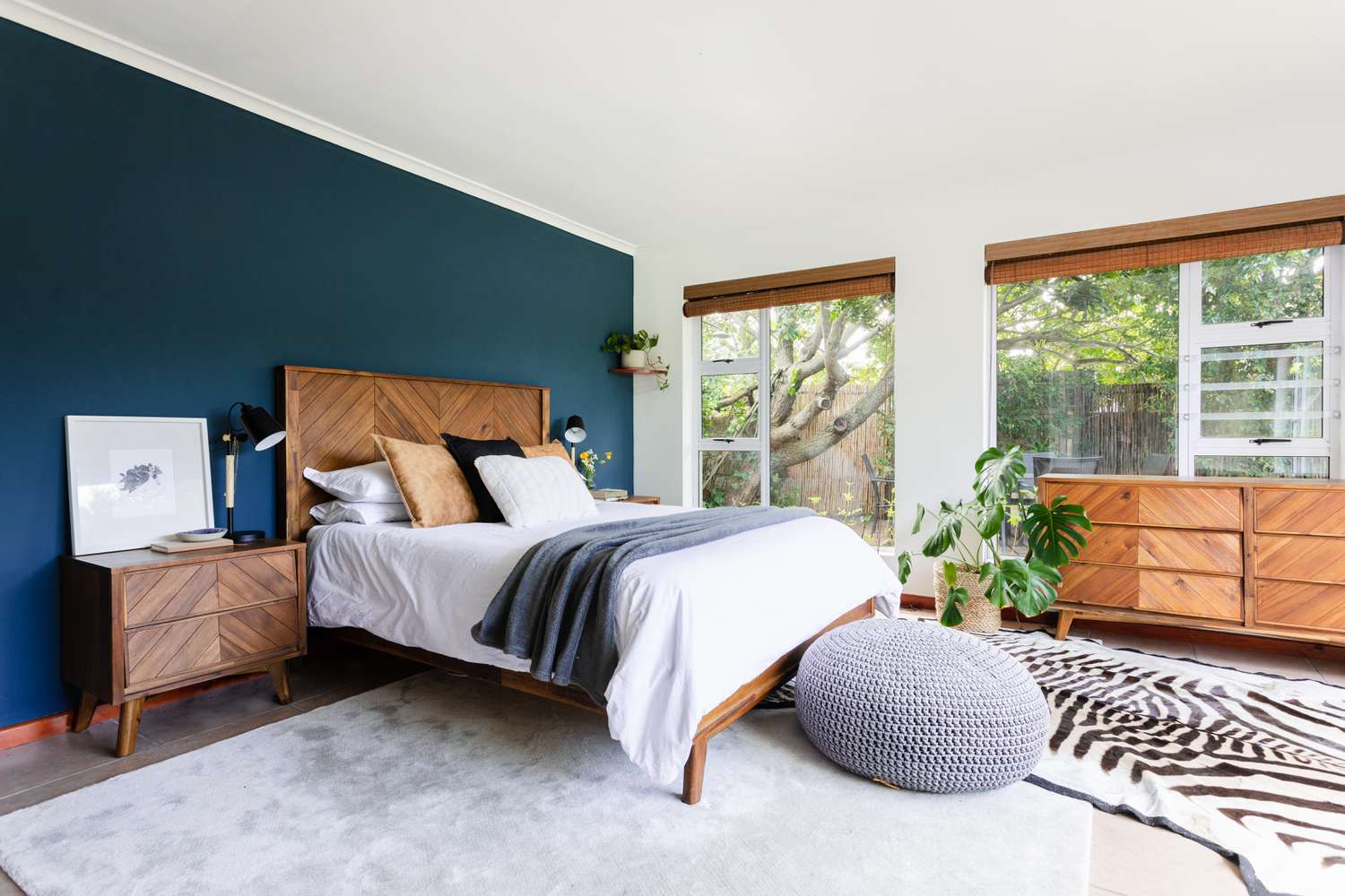 Schlafzimmer mit marineblauer Wand, modernen Mid-Century- und Holzmöbeln und großen Fenstern