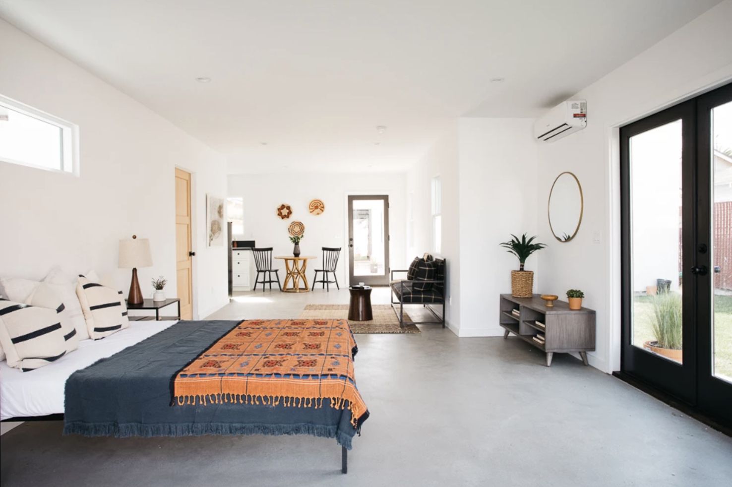quarto com layout aberto, colcha azul-marinho, piso de concreto, luz natural