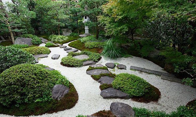 Steine und Moos bilden einen Weg durch weißen Kies in einem japanischen Garten.