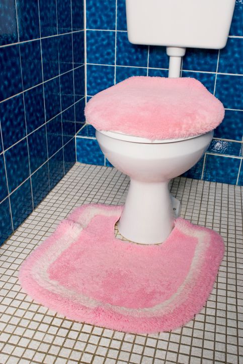 Unscharfer rosa Toilettensitzbezug und Matte im Badezimmer mit blauen und weißen Fliesen