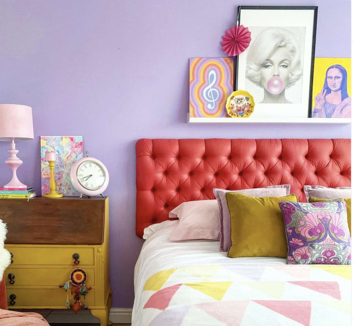 quarto eclético de cores vivas com paredes roxas, edredom de padrão triangular, cômoda amarela estilo vintage