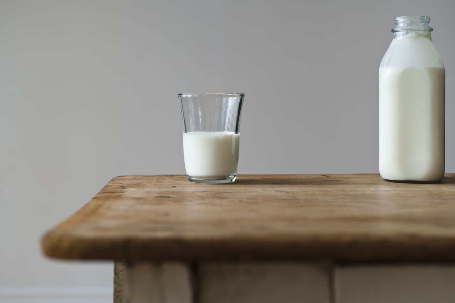 Quart de lait dans une bouteille en verre et un verre de lait à moitié plein sur une table en bois