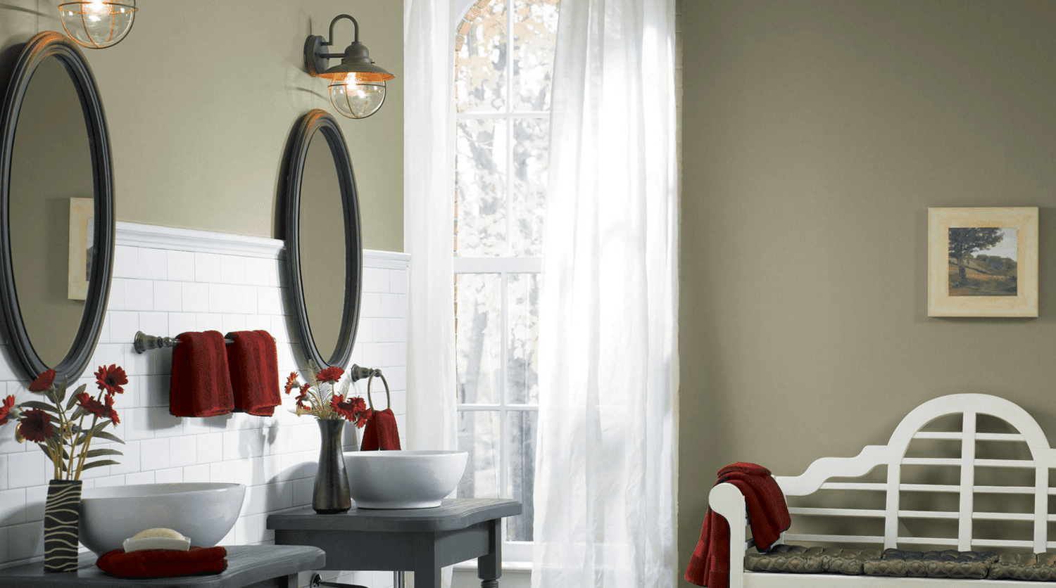 Ein schönes Badezimmer mit braunen Wänden, weiß gestrichenen Möbeln und zwei ovalen Spiegeln.