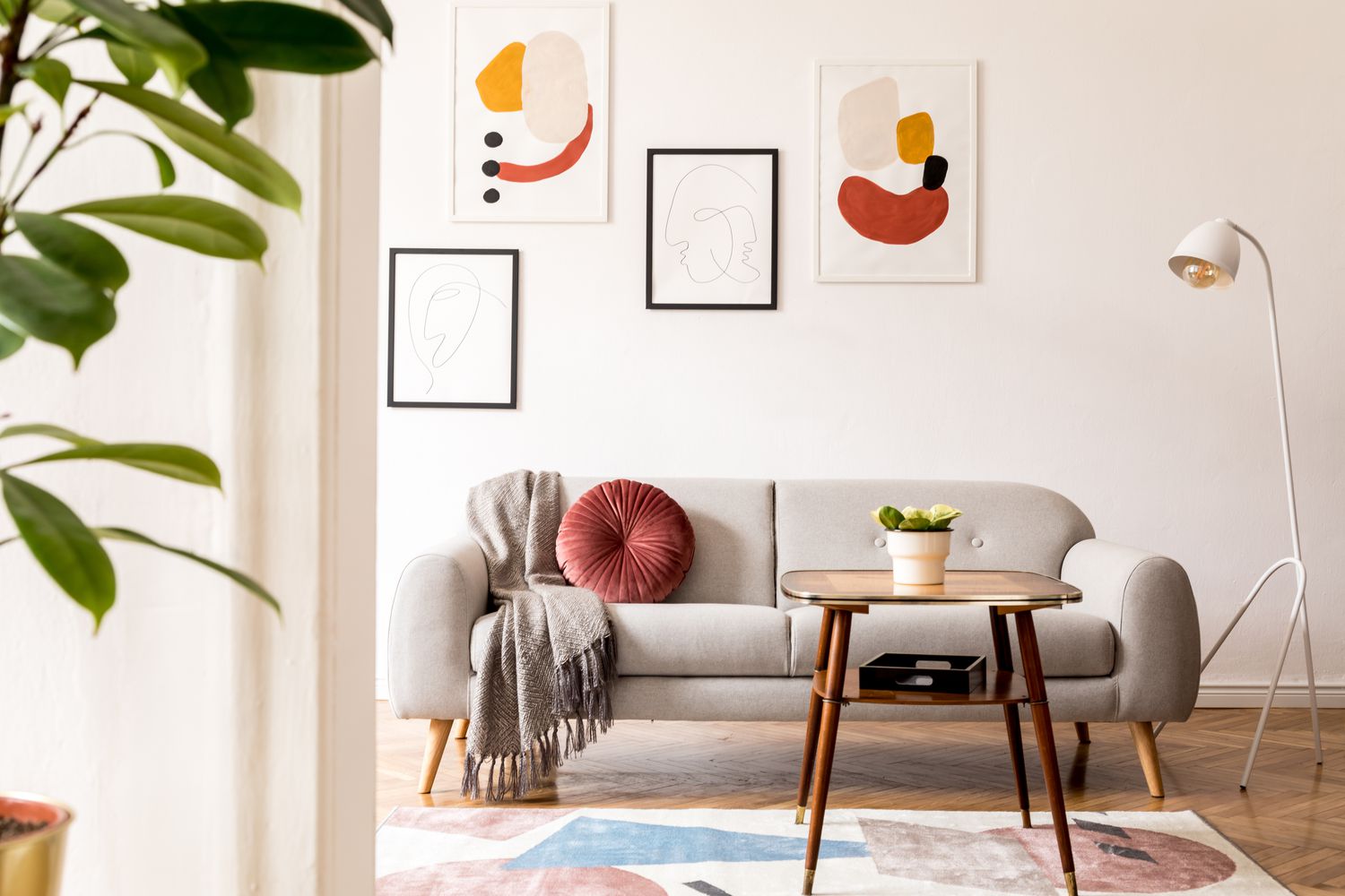 Uma sala de estar branca com detalhes neutros e pinturas abstratas coloridas penduradas atrás do sofá
