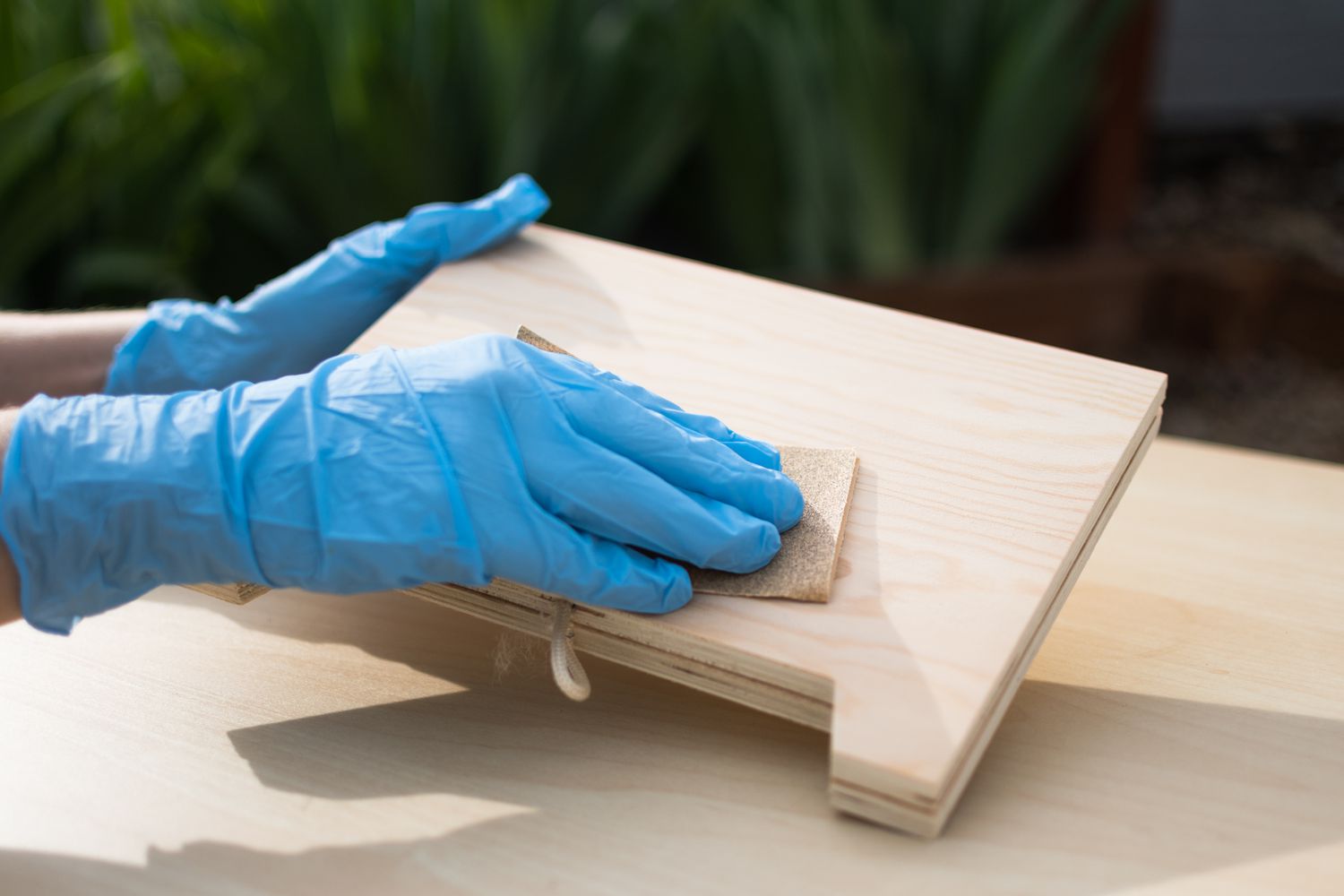 Holzschild mit feinem Schleifpapier und blauen Handschuhen abgeschliffen