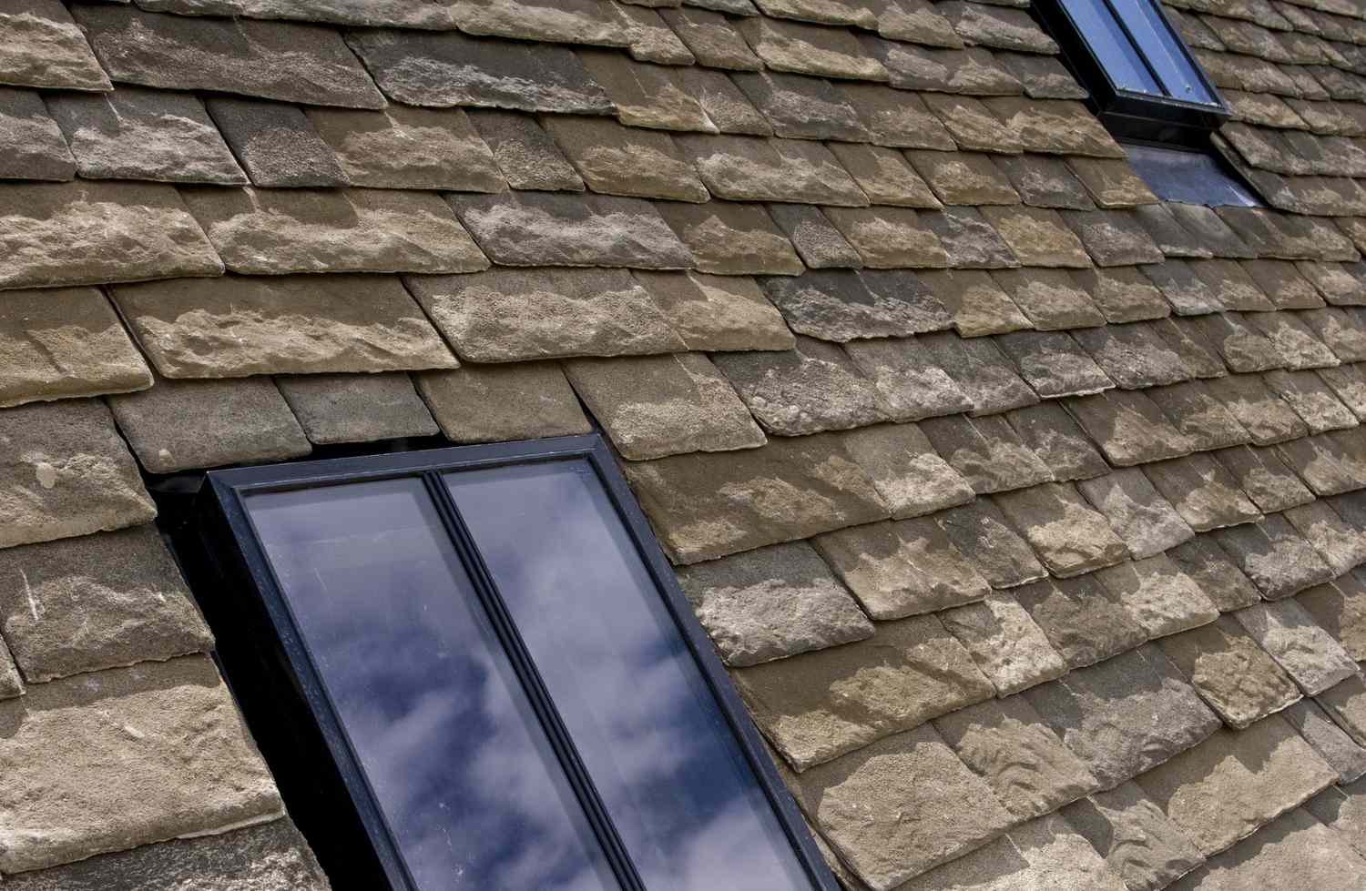 Detail von Dachschindeln, die wie Schiefer aussehen und doppelverglaste Oberlichter umgeben