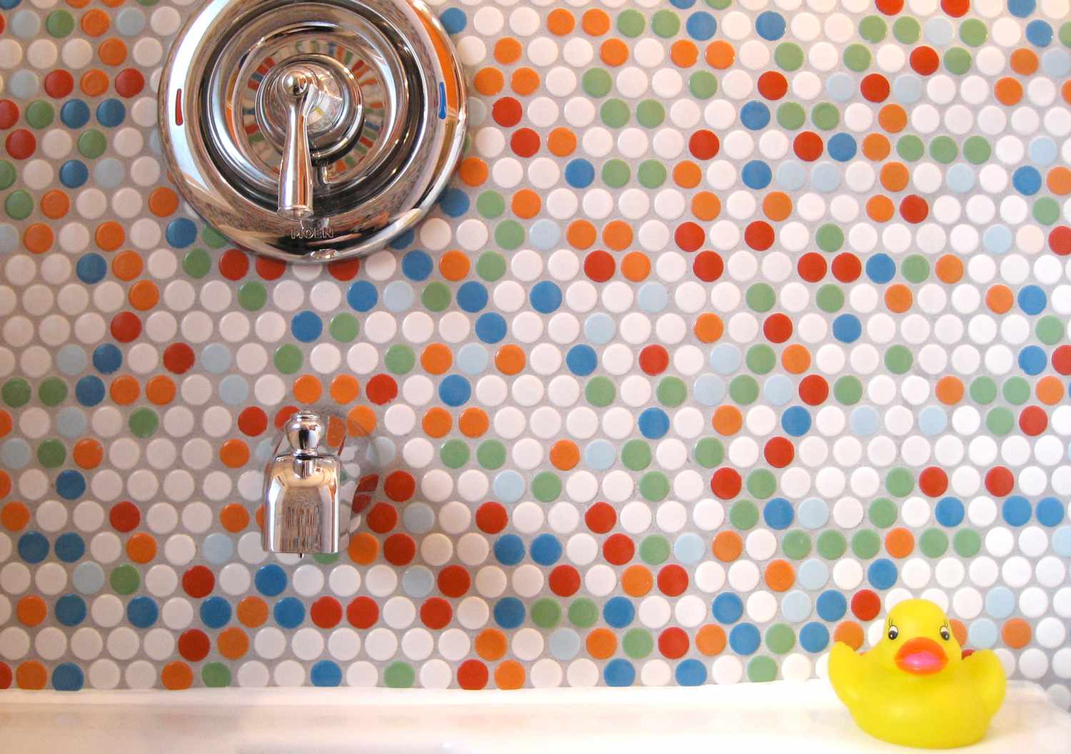 Round rainbow tile on bathtub wall with a rubber duck in front