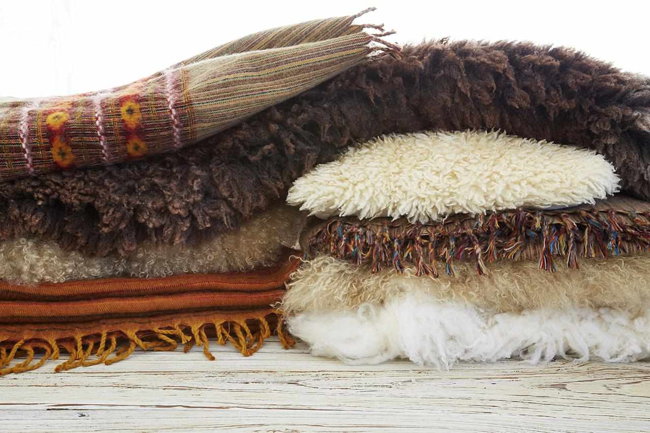 Natureza morta de cobertores tibetanos de lã, travesseiros e tapetes de pele sobre mesa de madeira