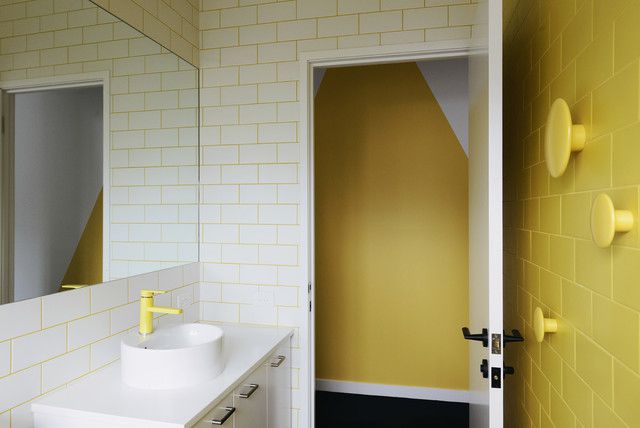 Banheiro e espelho com uma parede de azulejos amarelos acentuados e paredes de azulejos brancos com rejunte amarelo