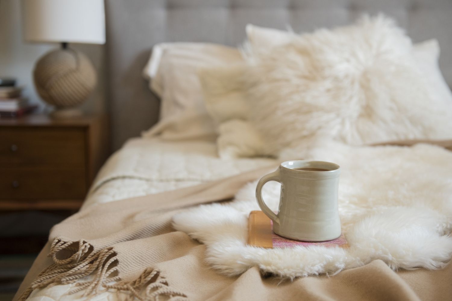Acogedora cama con lujosas mantas arrojadizas y un cubo de café encima de un libro.