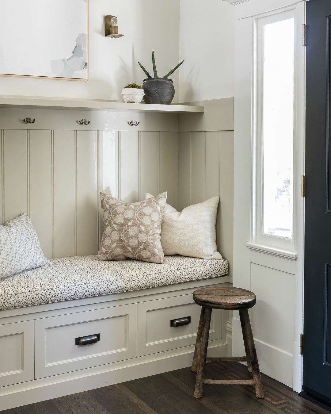 Un mudroom con banco de almacenaje empotrado, un cojín para el banco y cojines decorativos.