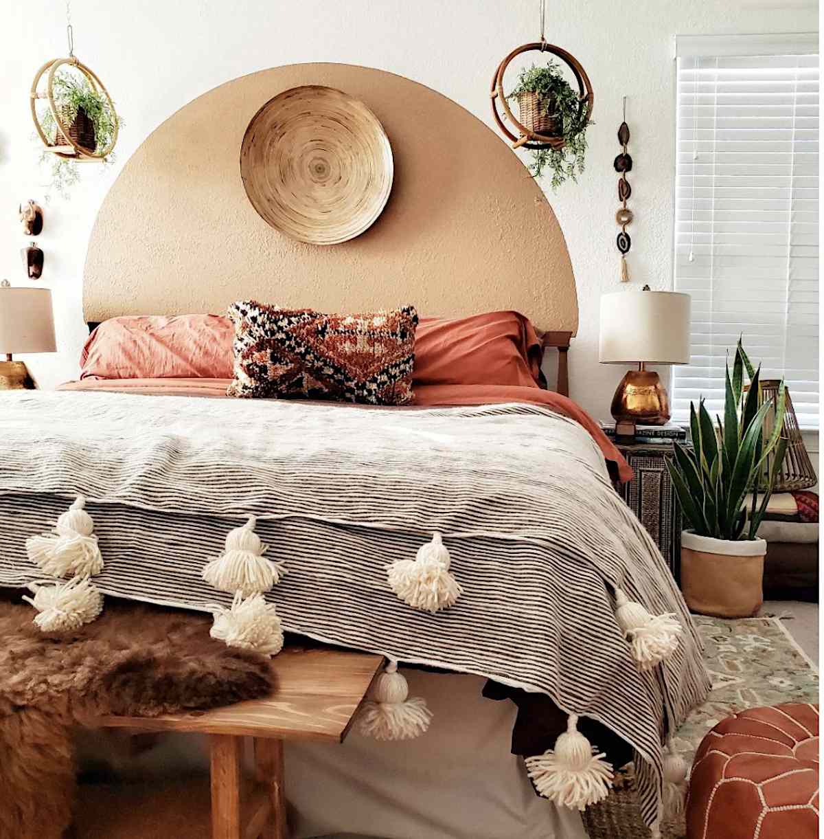 chambre de style boho avec rouge chaud, décorée avec des plantes, une peinture murale en demi-cercle sur la tête de lit
