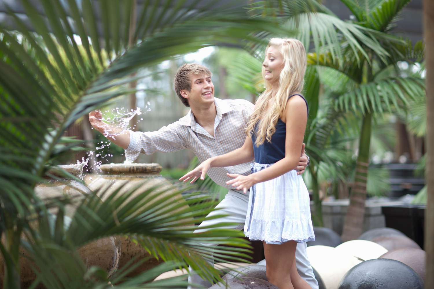 Pareja disfrutando del chorro de la fuente en el patio con palmeras.