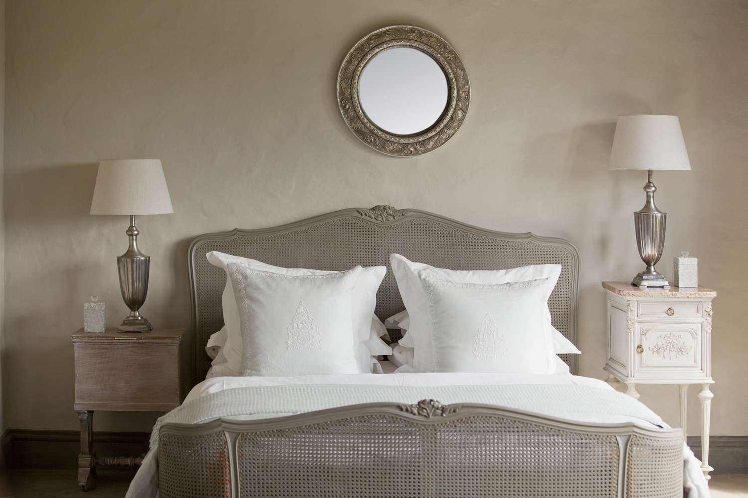 Dormitorio gris con cama, dos mesas auxiliares, dos lámparas y un espejo sobre la cama.