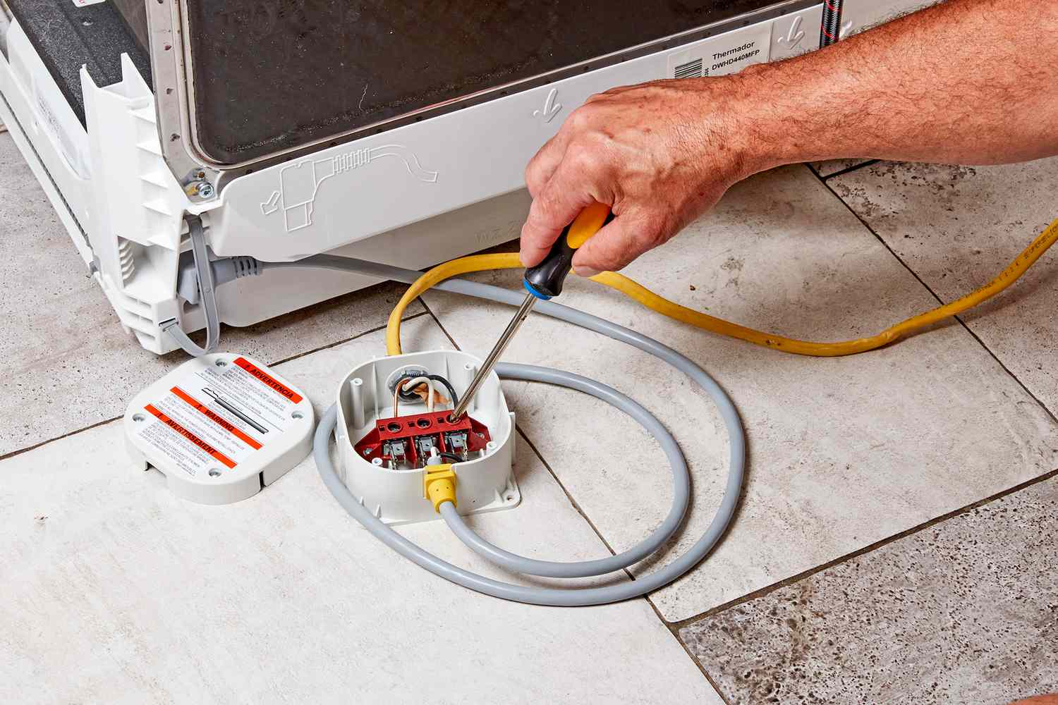 Caja de conexiones del cableado del lavavajillas abierta con destornillador asegurando el cable del circuito