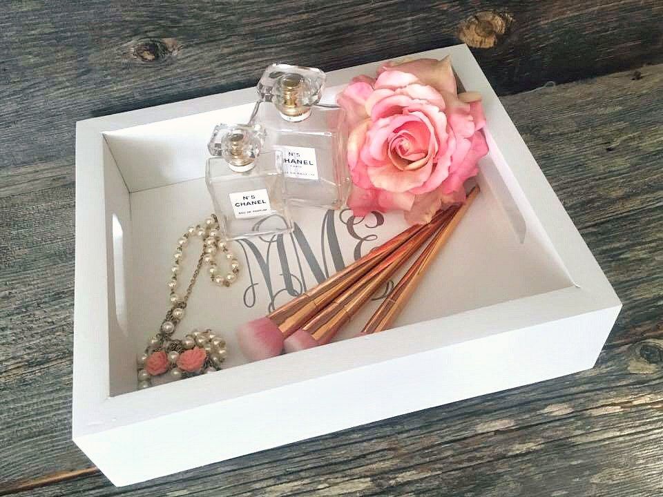 bandeja blanca con brochas de maquillaje, perfume, un collar y una flor