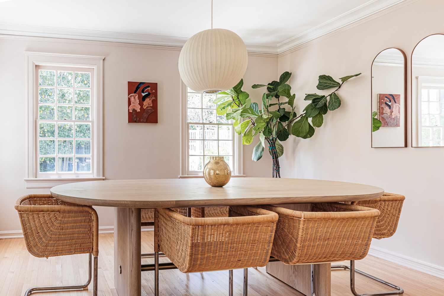 Sala de jantar com paredes pintadas em cor bege neutra com mesa oval e cadeiras de vime no centro