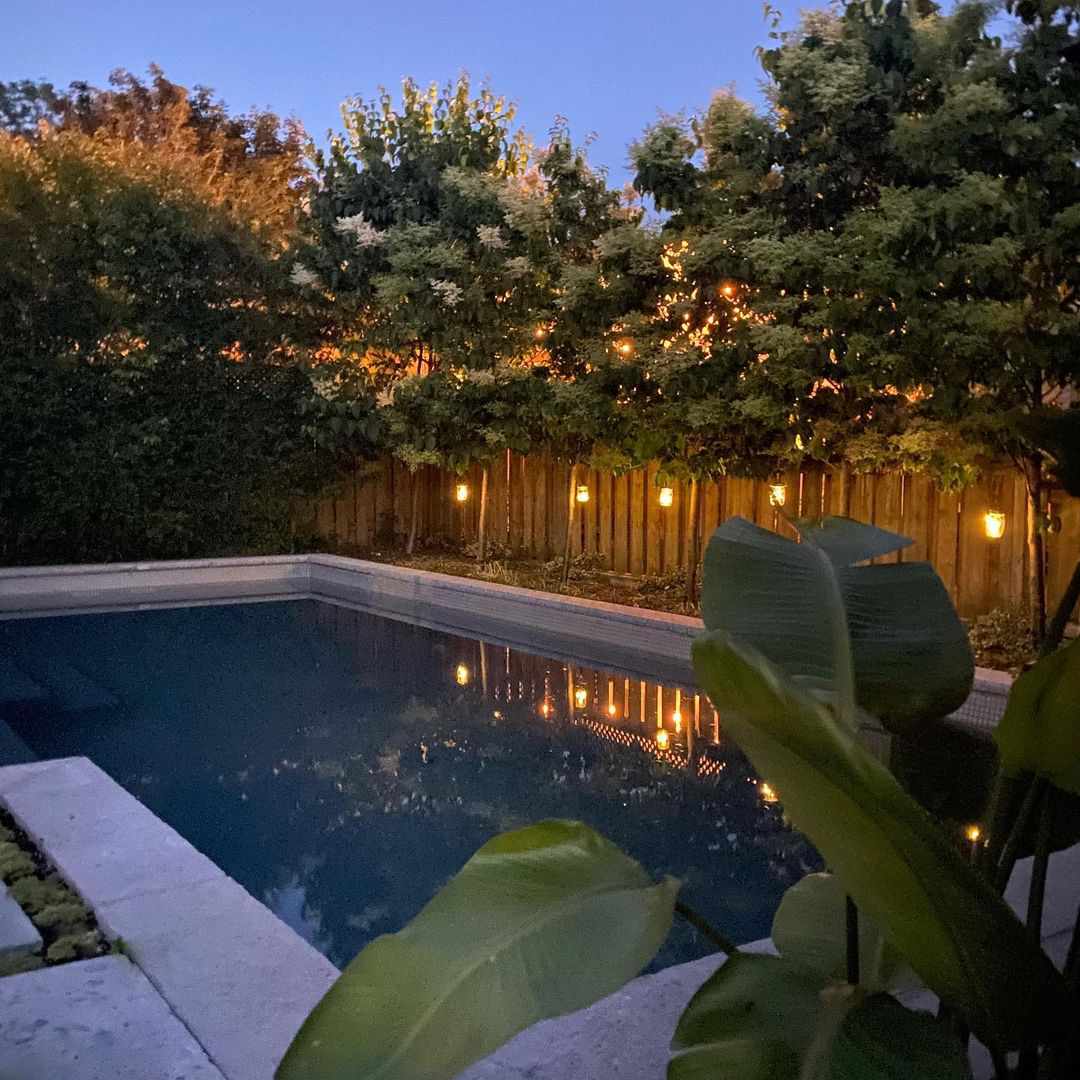 Uma piscina de quintal ao anoitecer com lanternas penduradas na cerca.