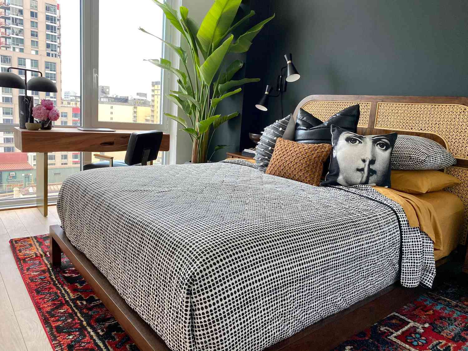 Braunes und schwarzes modernes Schlafzimmer mit großer Pflanze, Kissen in verschiedenen Stilen, eklektischer Teppich