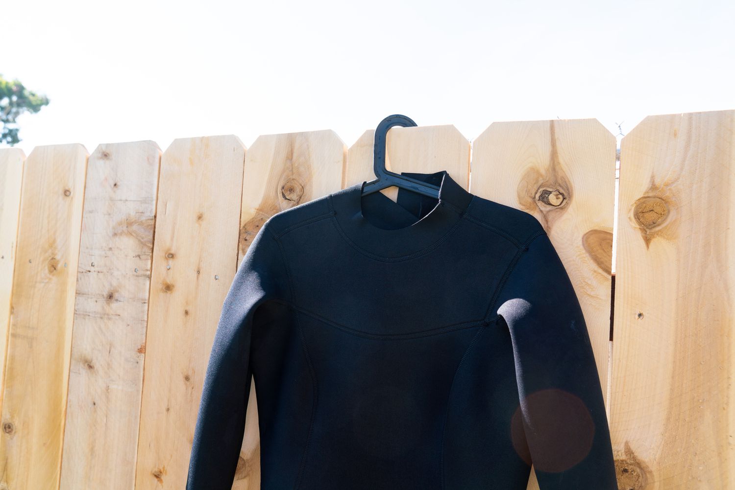 Heavy padded hanger in black wet suit hanging on wooden fence to air dry