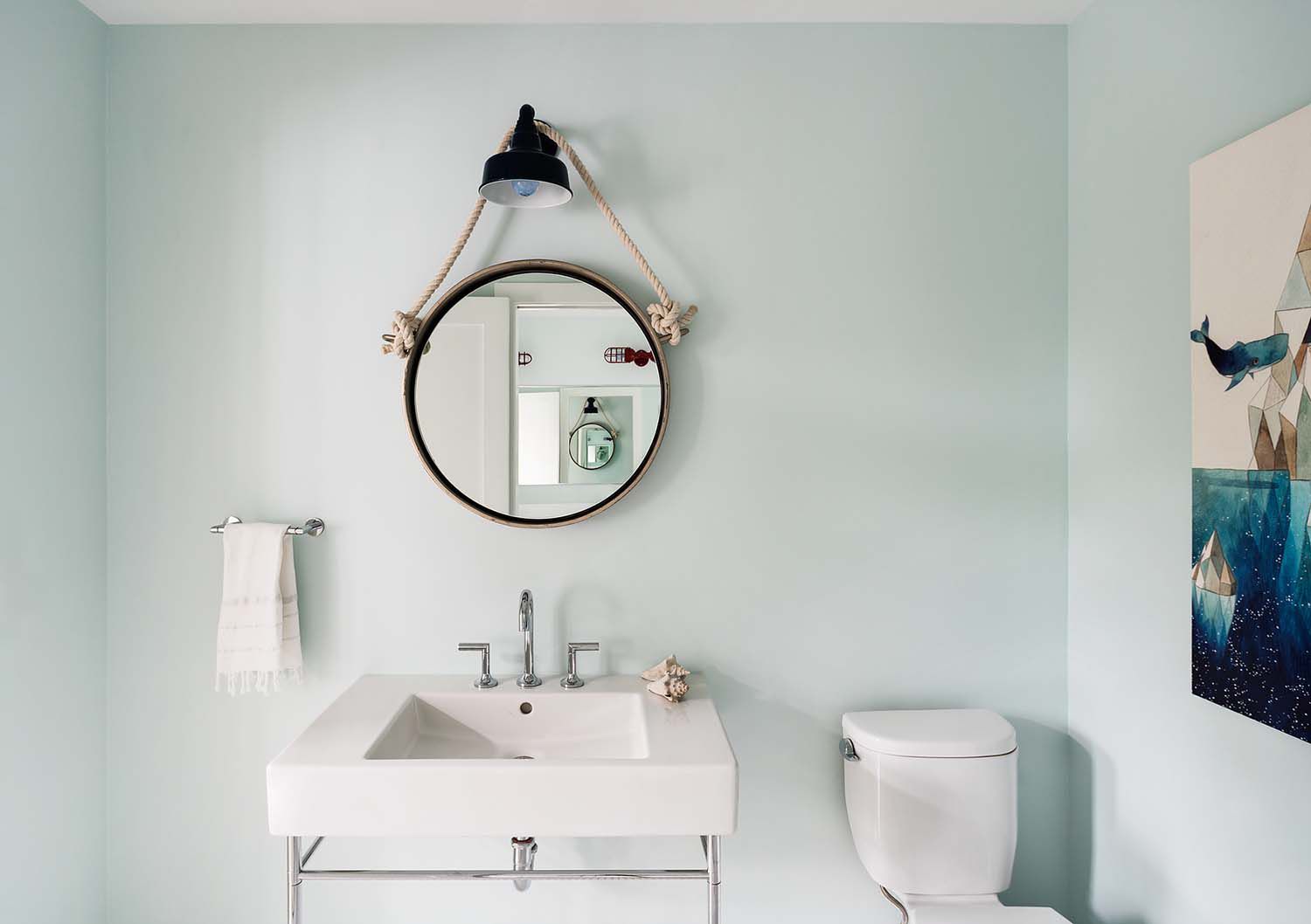banheiro discreto de inspiração náutica com espelho redondo