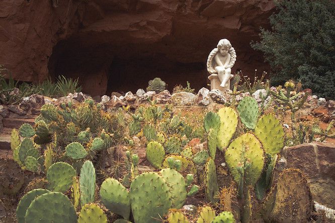 Engelsskulptur in einem großen Kakteengarten vor dem Eingang einer Felsenhöhle