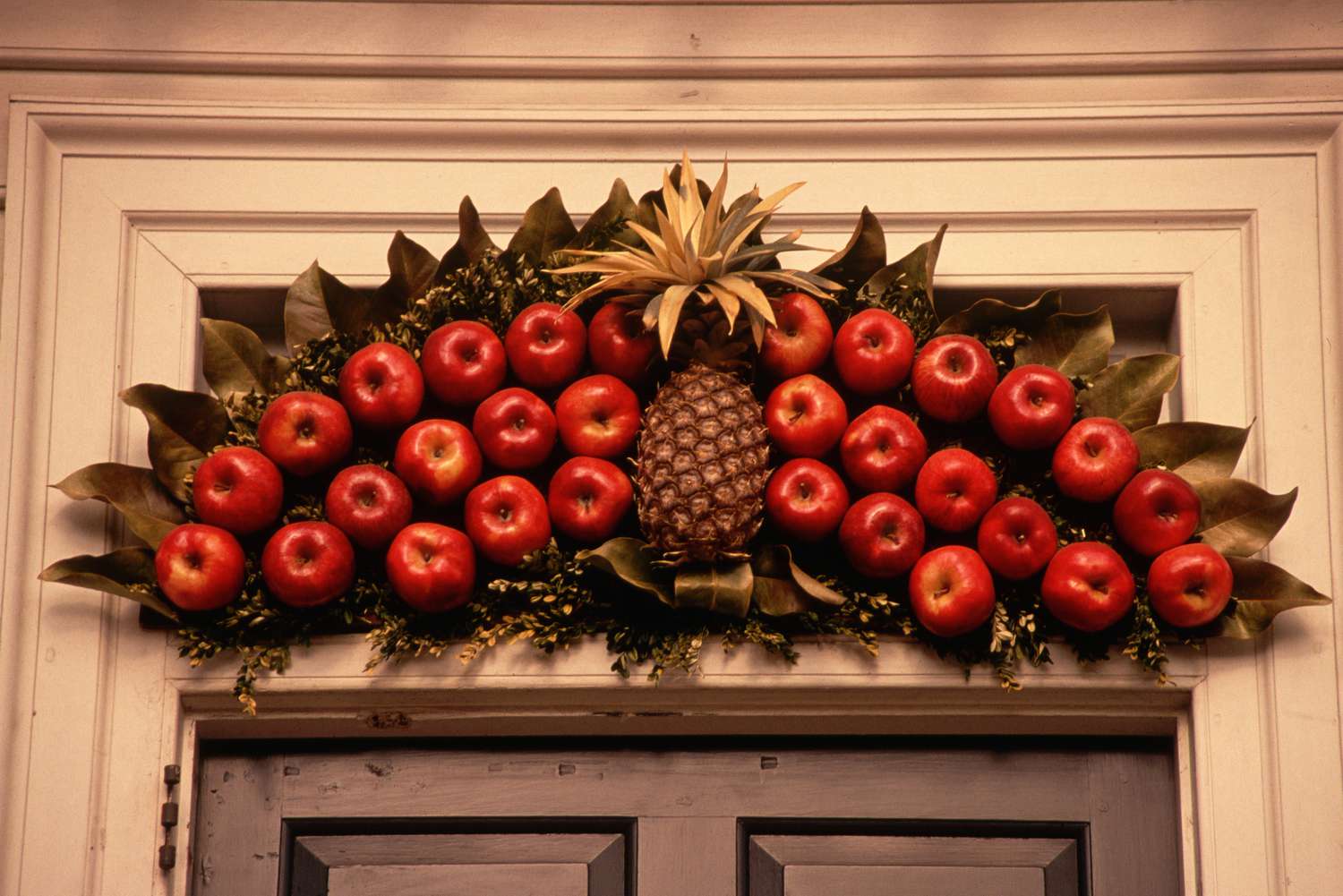 Frutas (manzanas y una piña) expuestas sobre una puerta como decoración navideña al aire libre.