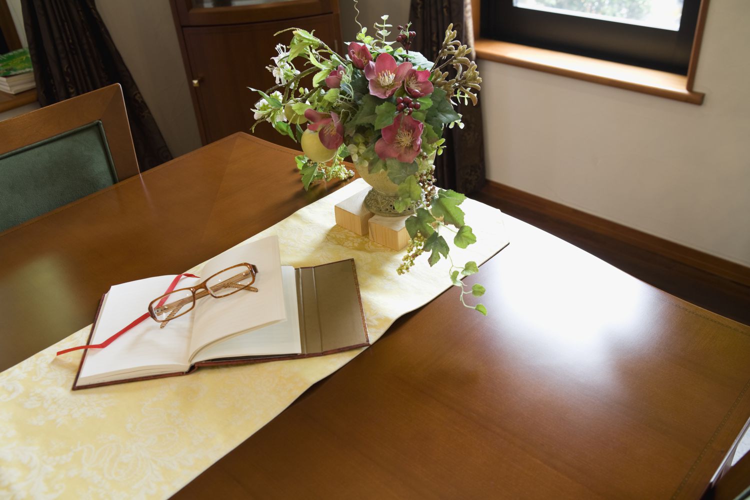 Arranjo de flores falsas em uma mesa de madeira com livro e copos