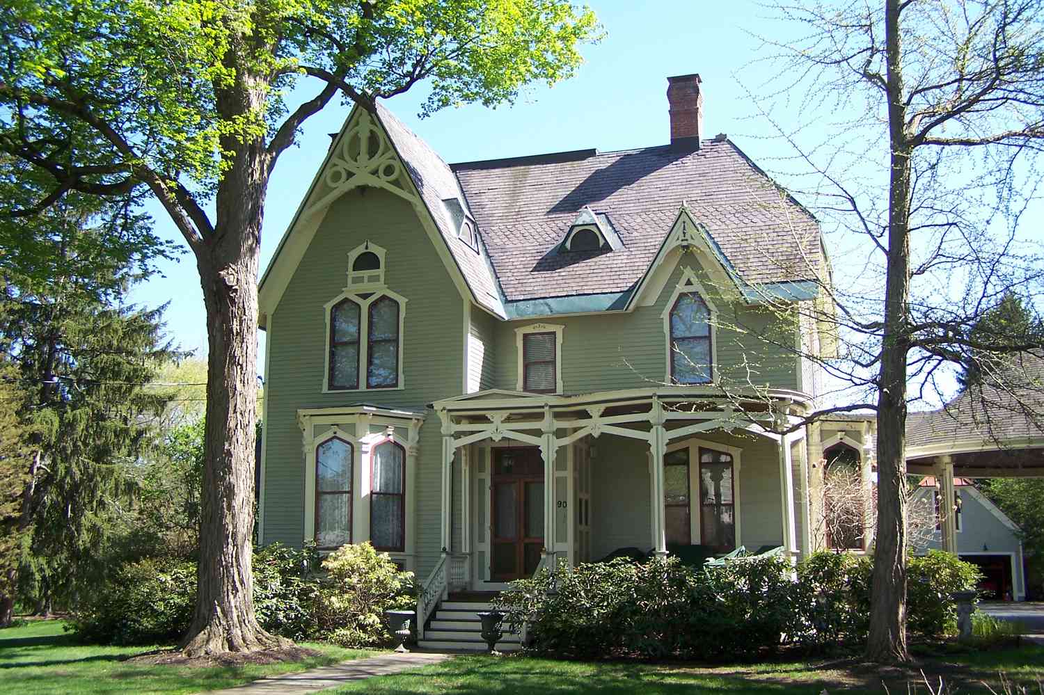 Casa victoriana de dos plantas, revestimiento verde con ribetes crema y rojo, tejado empinado con frontones y remates de bargeboard