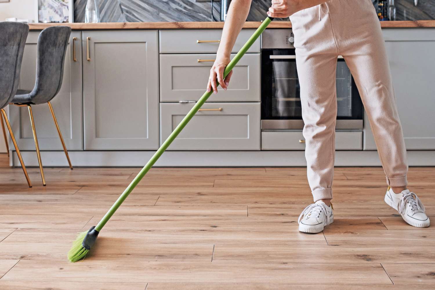 Wooden floors being sweep with a green broom in kitchen with gray cabinets