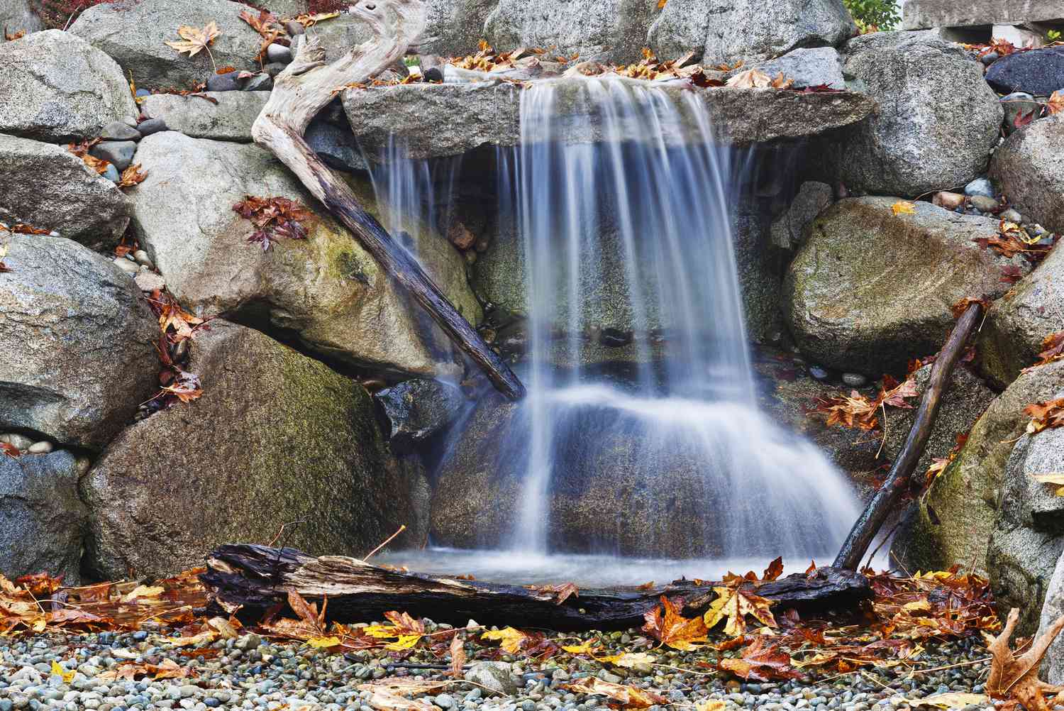 Cascada de piedra de aspecto natural con ramas y hojas caídas.