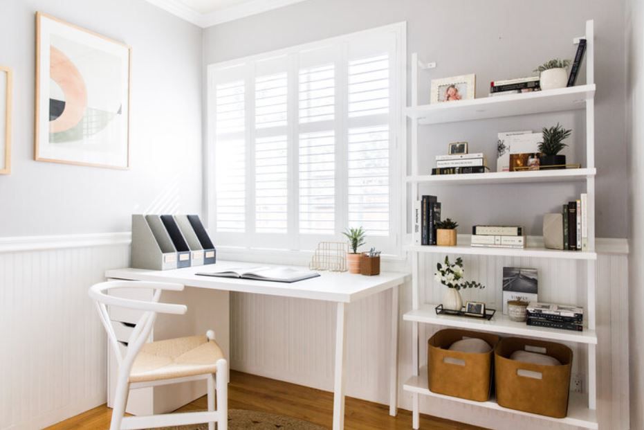 Heimbüro mit weißem Schreibtisch und Bücherregalen und offenem Buch auf dem Schreibtisch.