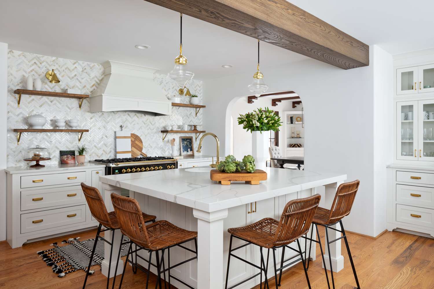Die weiße Küche im Haus von Erin Coren zeichnet sich durch einen Holzbalken, weiße Schränke und goldene Beschläge und Spüle aus