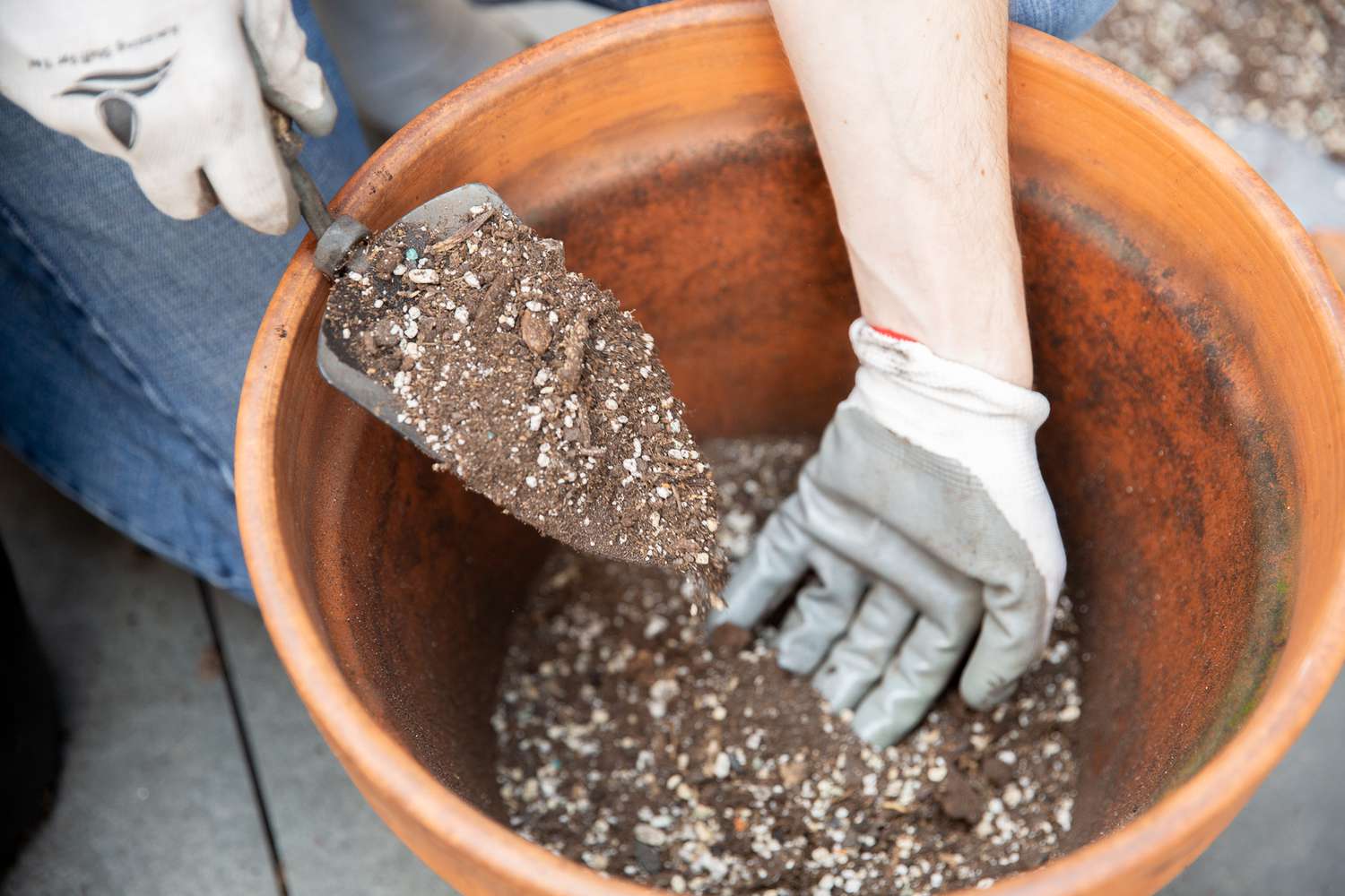 Blumenerdegemisch, das mit einer kleinen Handschaufel in einen großen Tontopf gegeben wurde 