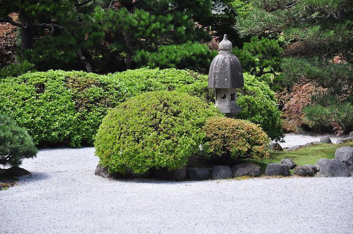 Zen-Garten mit Sträuchern, Kiesweg und Steinstatue.