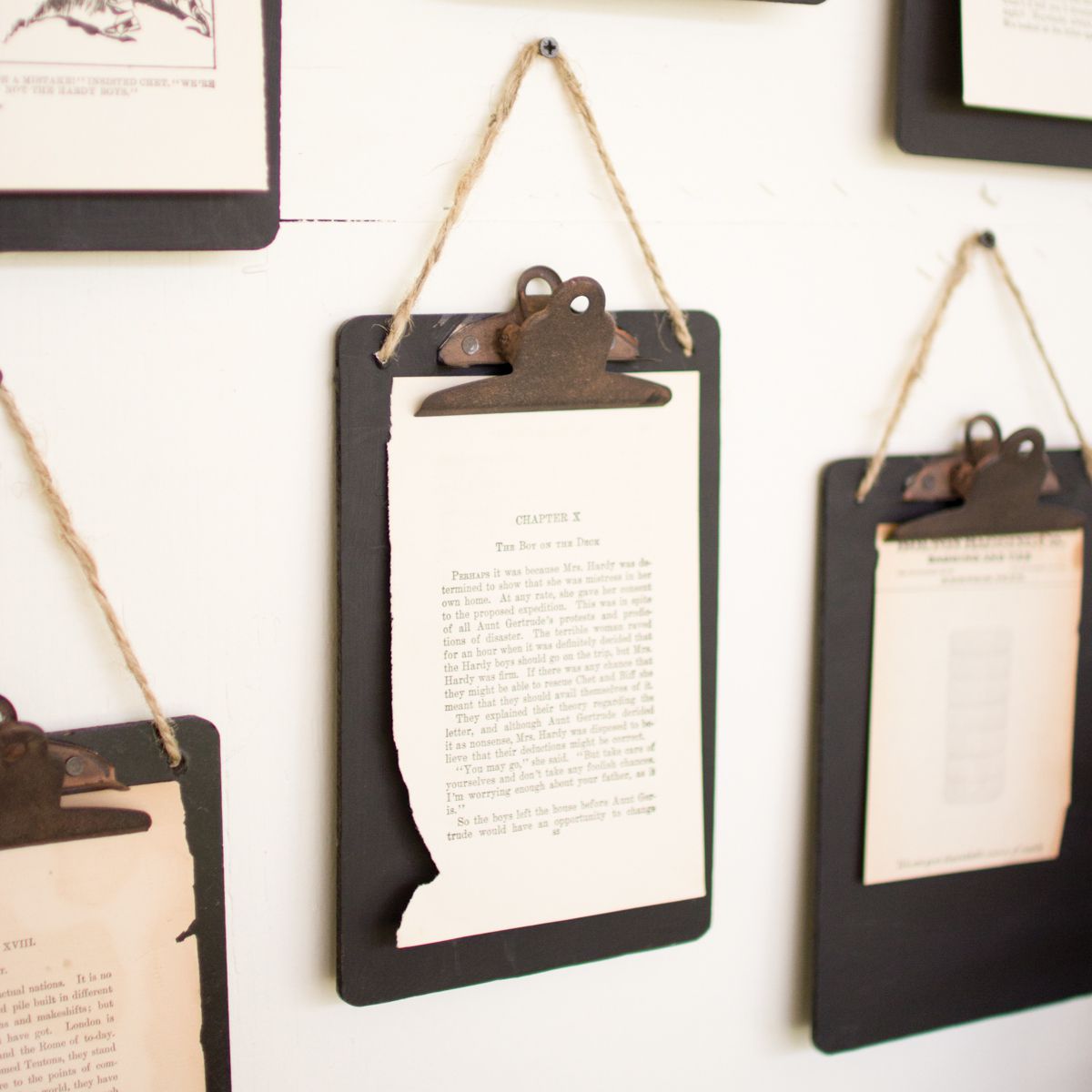 Planches à pince noires rustiques avec des pages de livres accrochées sur un mur blanc avec de la ficelle et des clous