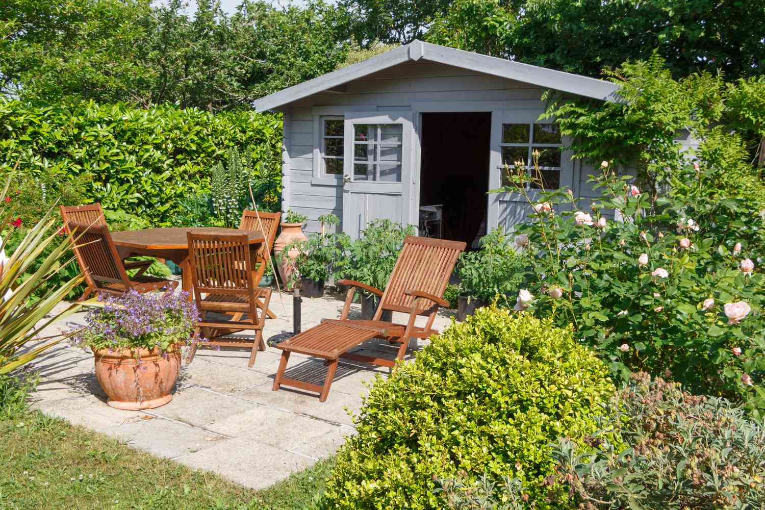 Abri de jardin avec des chaises longues, une table à manger, et beaucoup d'arbustes verts.