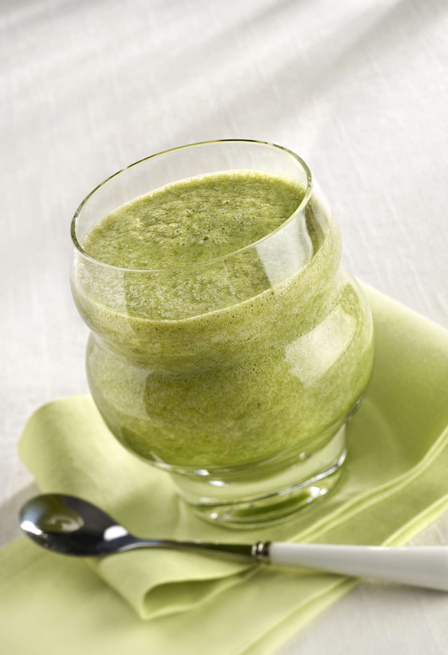 Green smoothie in a bulbous glass on a green cloth with a spoon