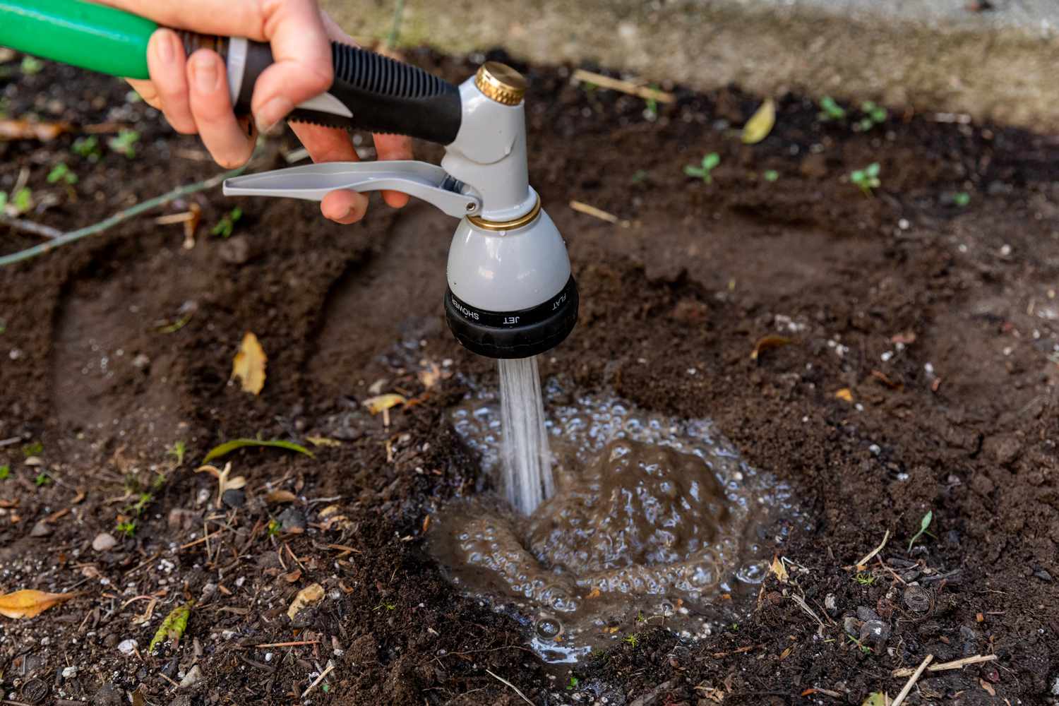 Wasser aus einem Schlauch, das in ein Erdloch gegossen wird, um die Drainage des Bodens zu testen